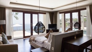 A hotel room with a bed, a desk, a TV, and large windows with a view of the sea. - Villa Maiara (Ungasan)