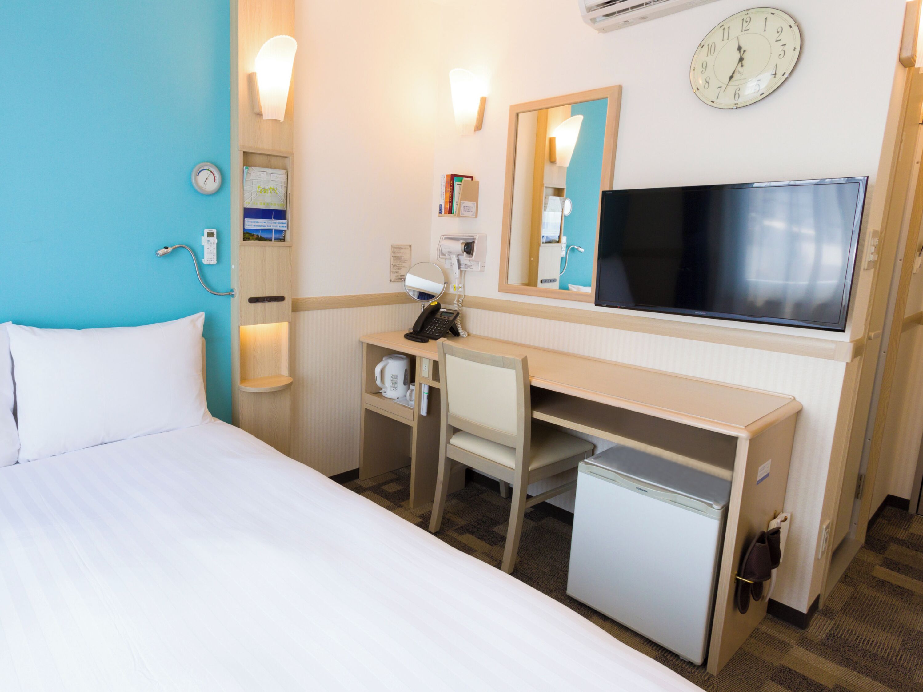 A hotel room with a bed, desk, chair, and a television.