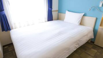 A neatly made bed in a hotel room with a blue wall and a bedside table with a lamp.