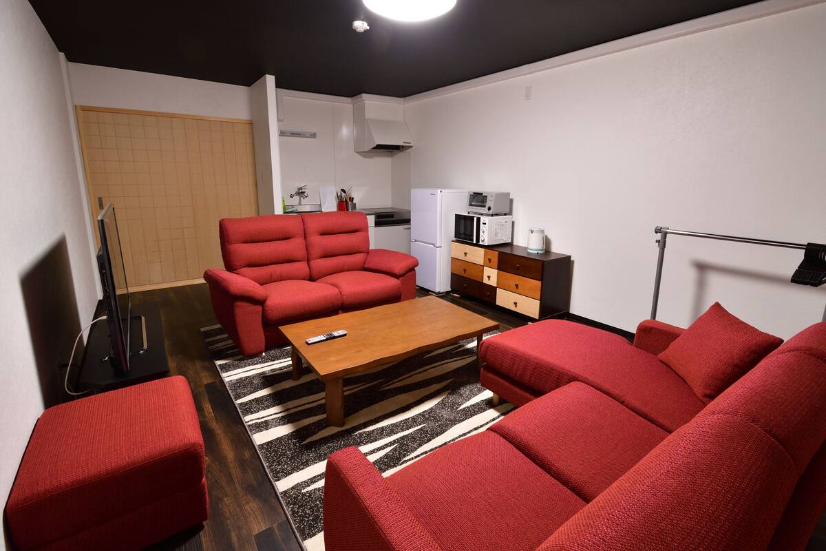 A compact living space with a sofa set, a coffee table, a kitchen area with a microwave and refrigerator, and a television.
