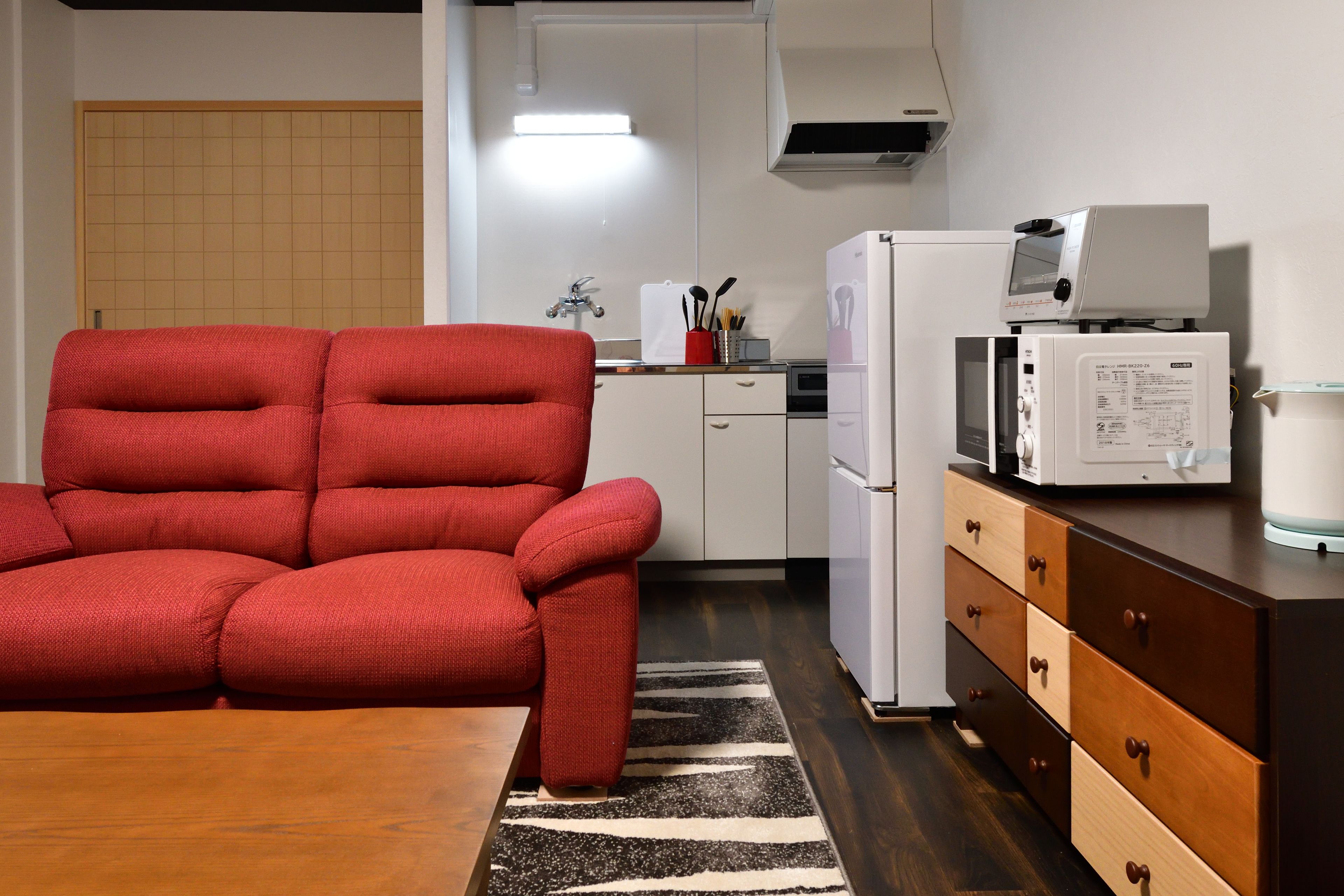 Una cocina compacta con microondas, refrigerador y un sofá rojo.
