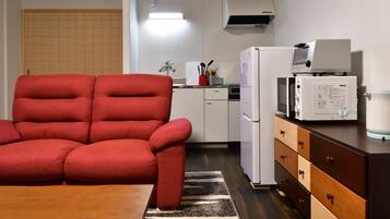 A compact kitchen with a microwave, refrigerator, and a red sofa.
