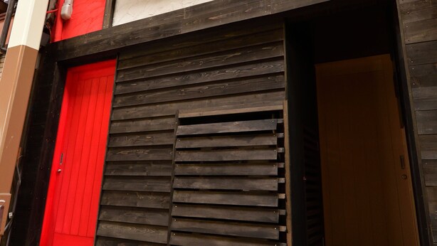 A building with a red door, a closed shutter, and a staircase leading to the entrance. - Machi de kurasu Tengachaya-2 (Osaka)