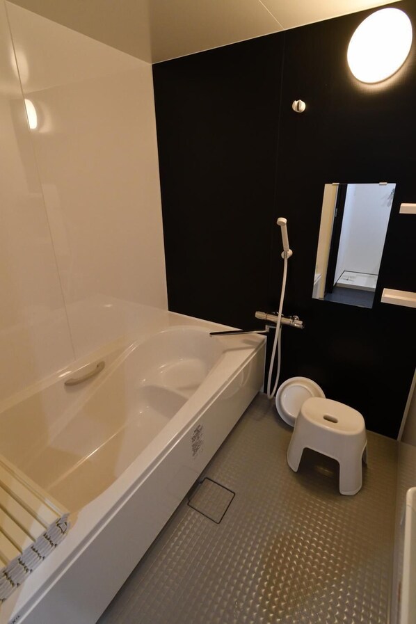 A modern bathroom with a bathtub, toilet, and a small stool.