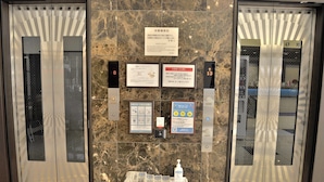 An elevator with a marble wall, two signs, and a small table with a bottle and papers.