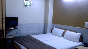 Una habitación de hotel con cama, televisor sobre un mueble y una mesita con teléfono.