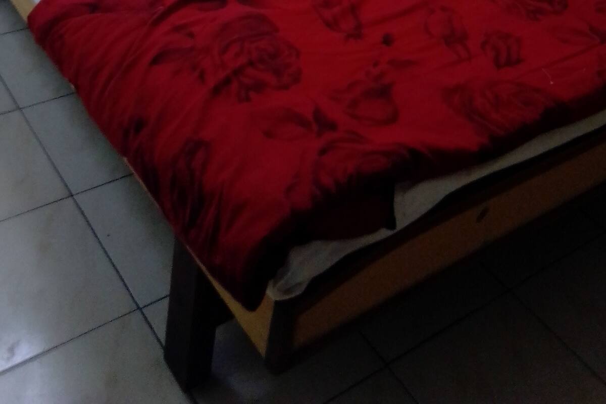 Uma cama de solteiro com roupa de cama branca e um cobertor floral vermelho.