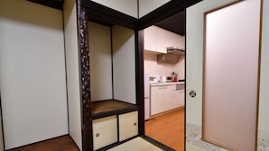 Habitació tradicional japonesa amb terra de tatami, porta corredissa de shoji i una cuina visible a través d'una porta oberta.