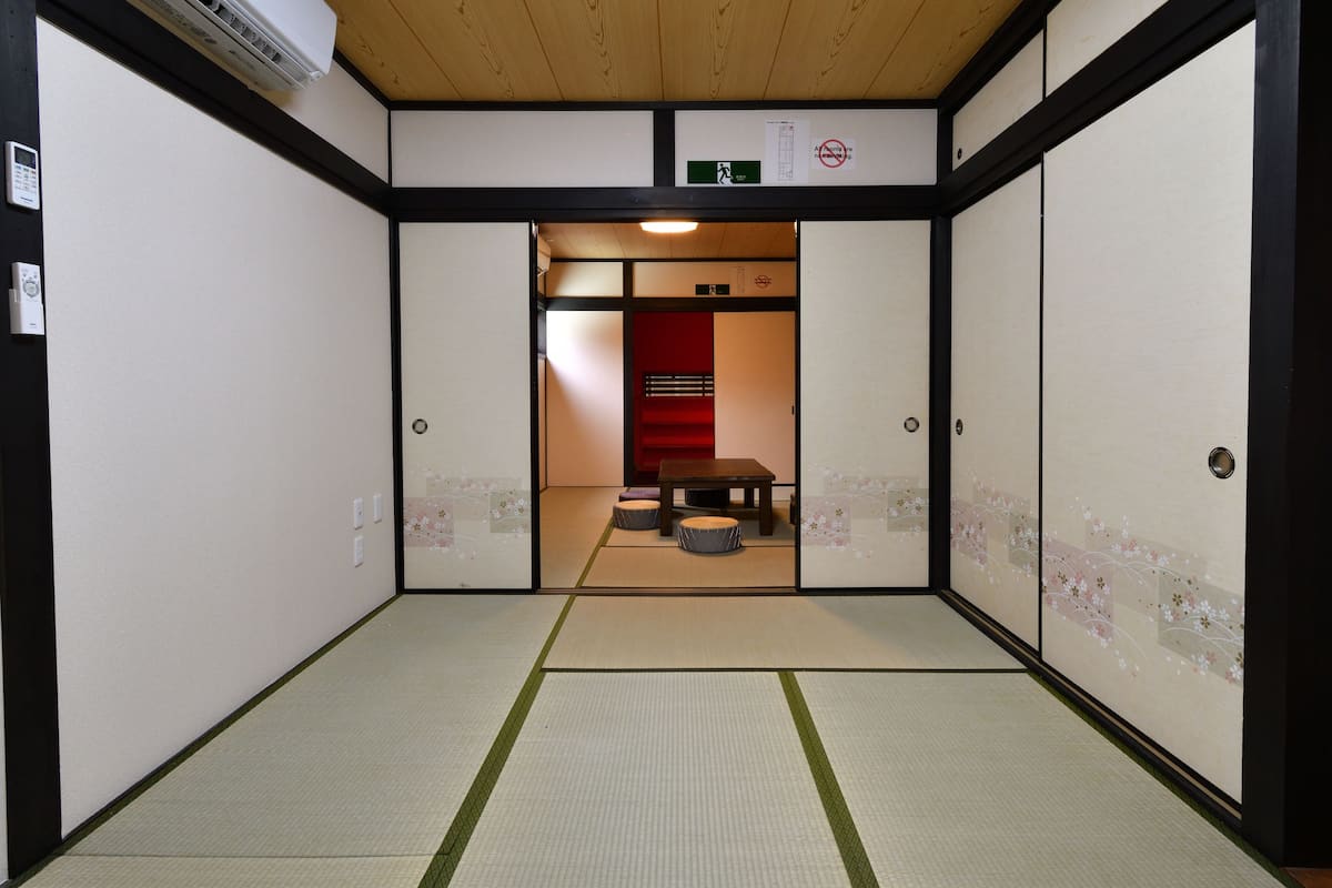 Una habitación japonesa tradicional con suelo de tatami, puertas correderas y una pequeña mesa con cojines.