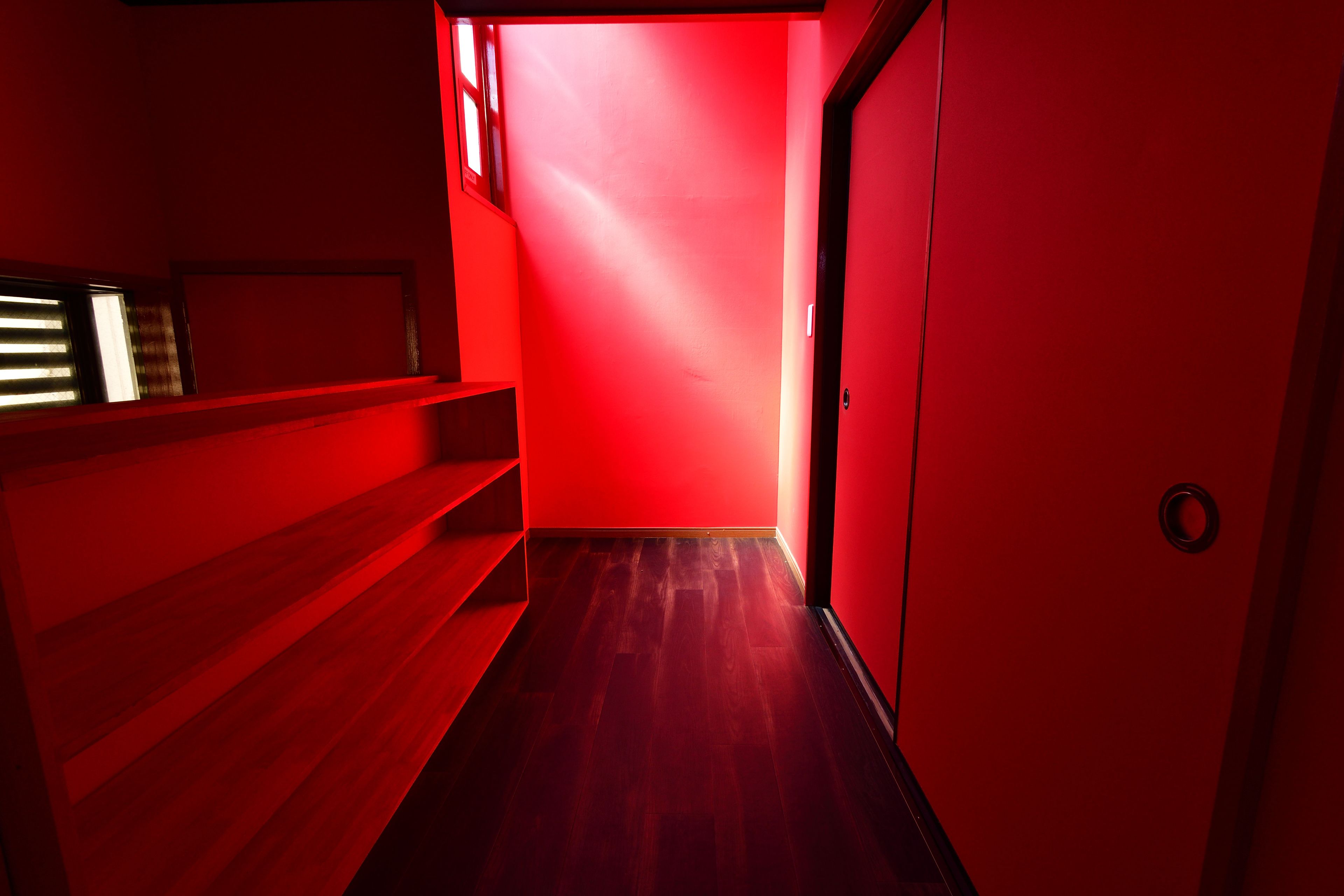 A narrow hallway with red walls and wooden flooring.