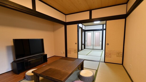 Habitació japonesa tradicional amb sòls de tatami, una taula de fusta baixa, televisió i una porta corredissa que dóna a una altra habitació.