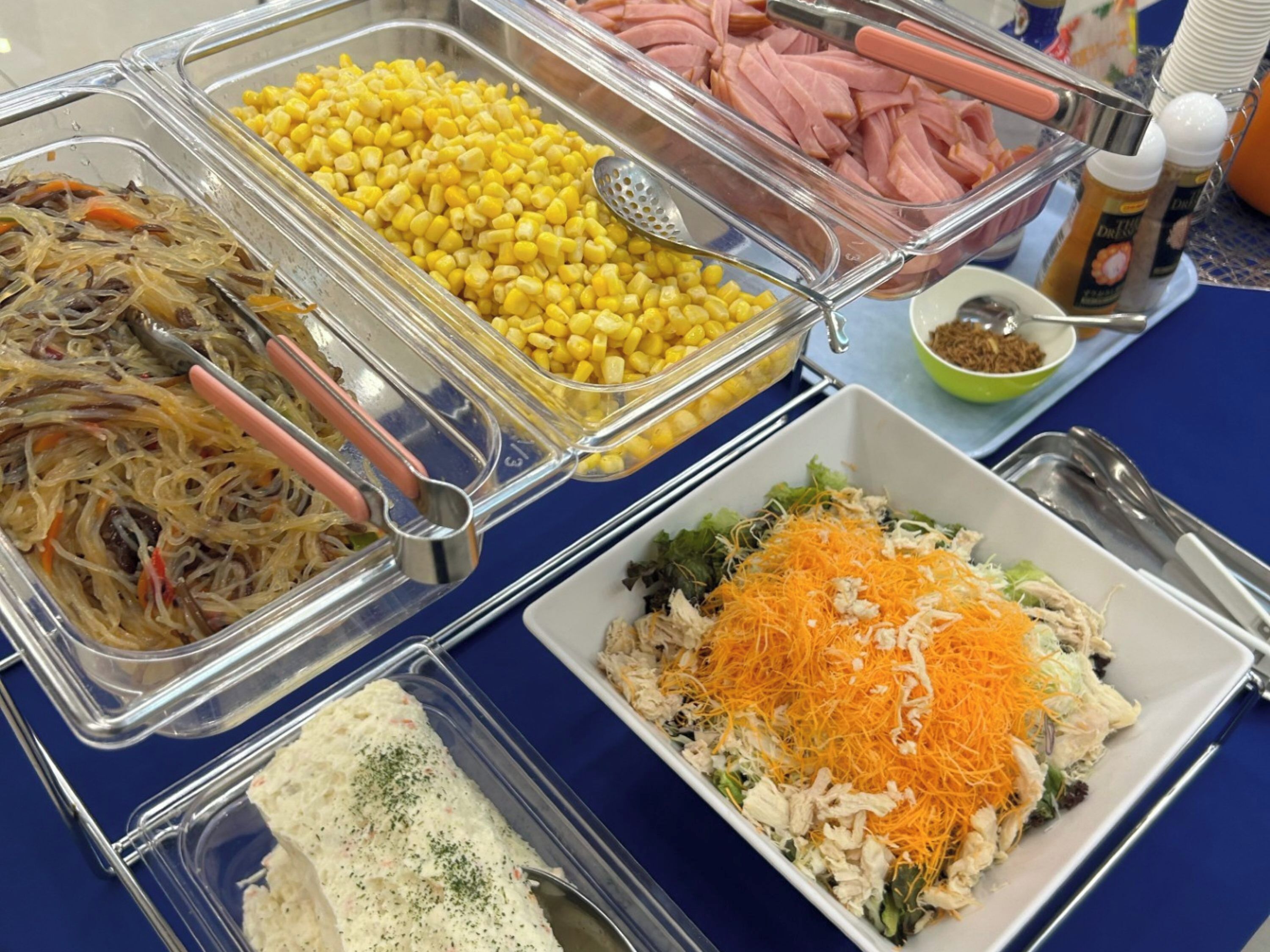 Un buffet proposant une variété de plats, notamment du maïs, du poulet effiloché et une salade avec du fromage râpé.