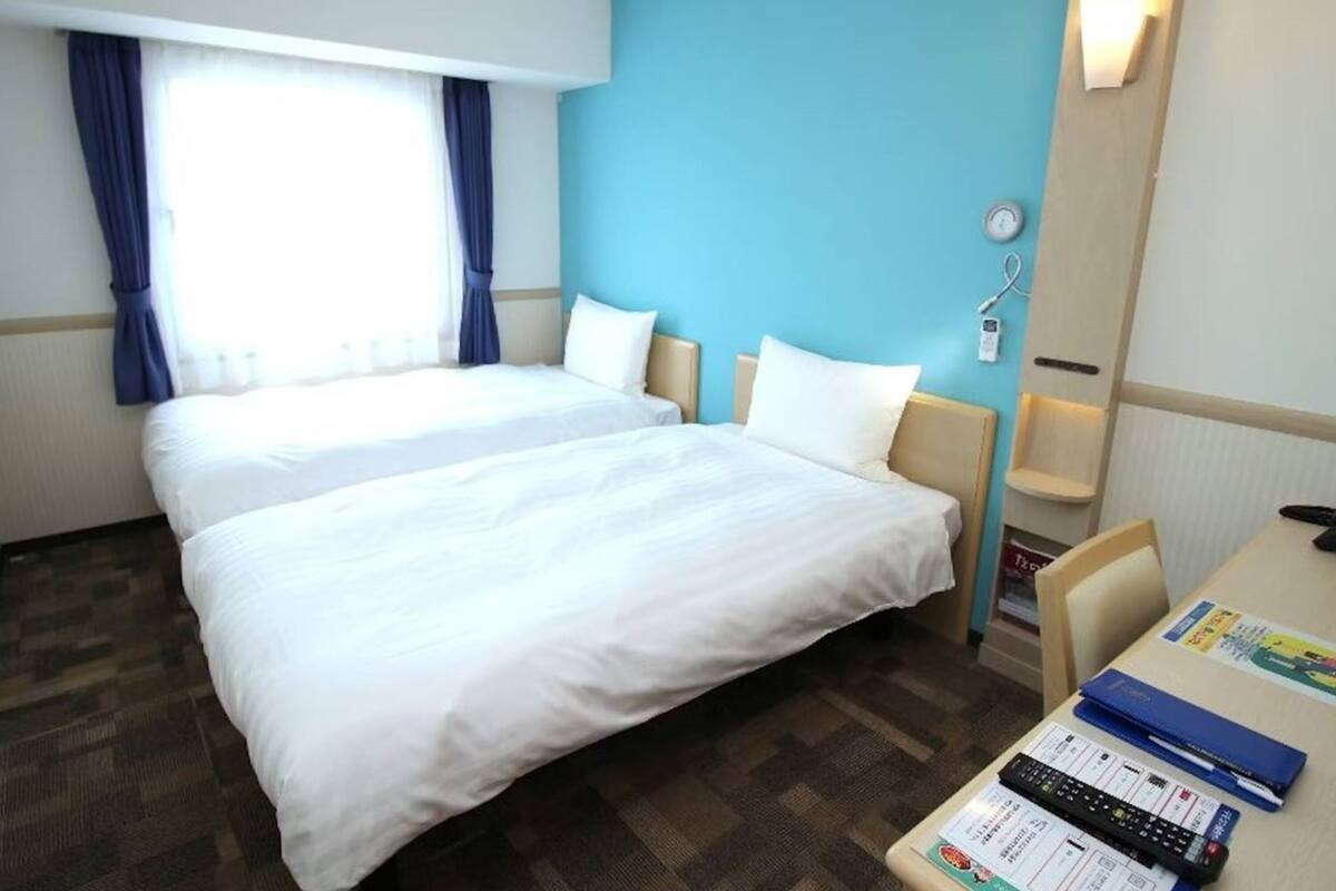 A hotel room with a large bed, a desk with a computer, and a window with curtains.