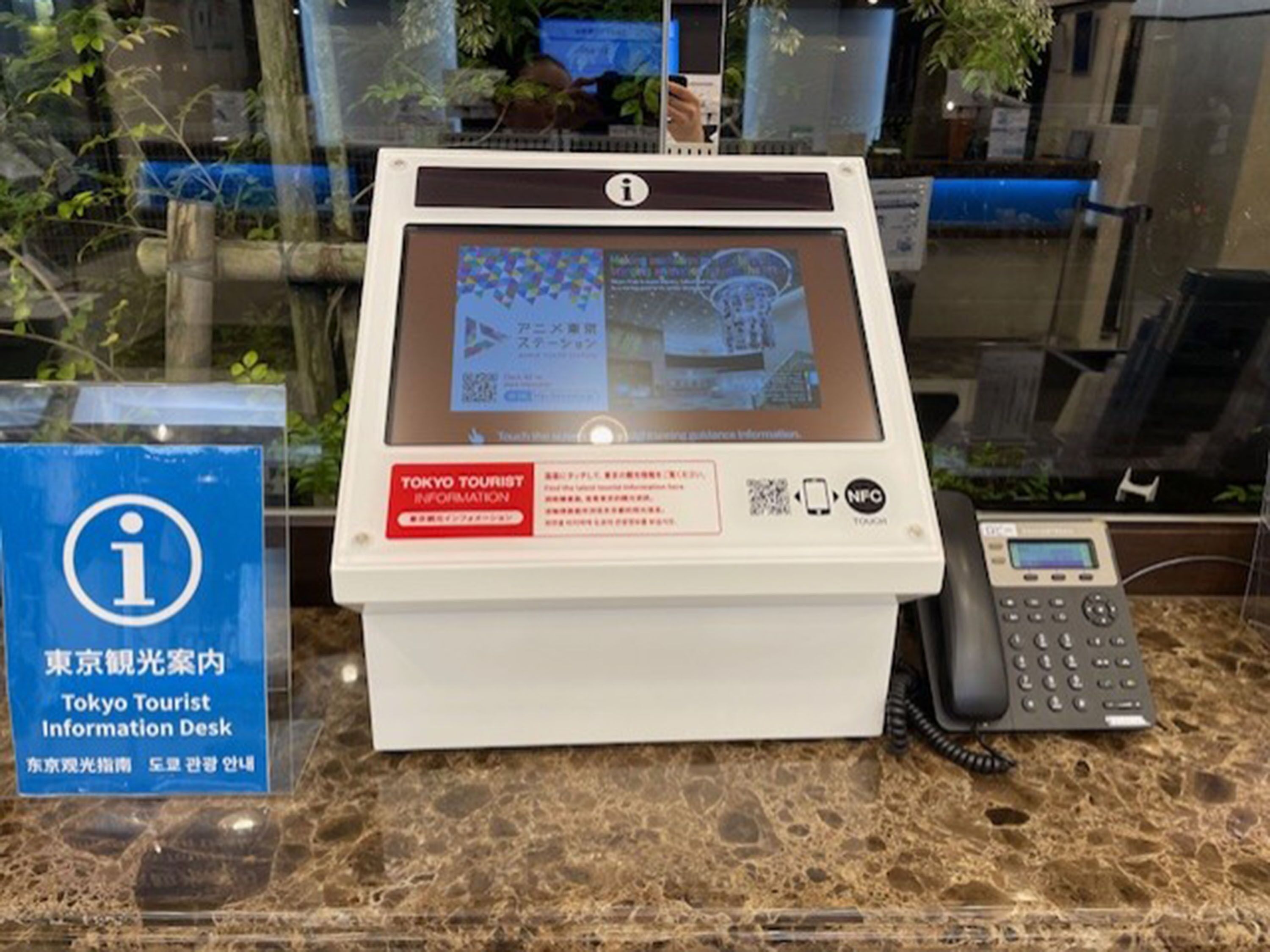 Un bureau d’information touristique à Tokyo, équipé d’un écran numérique, d’un téléphone et d’un code QR.