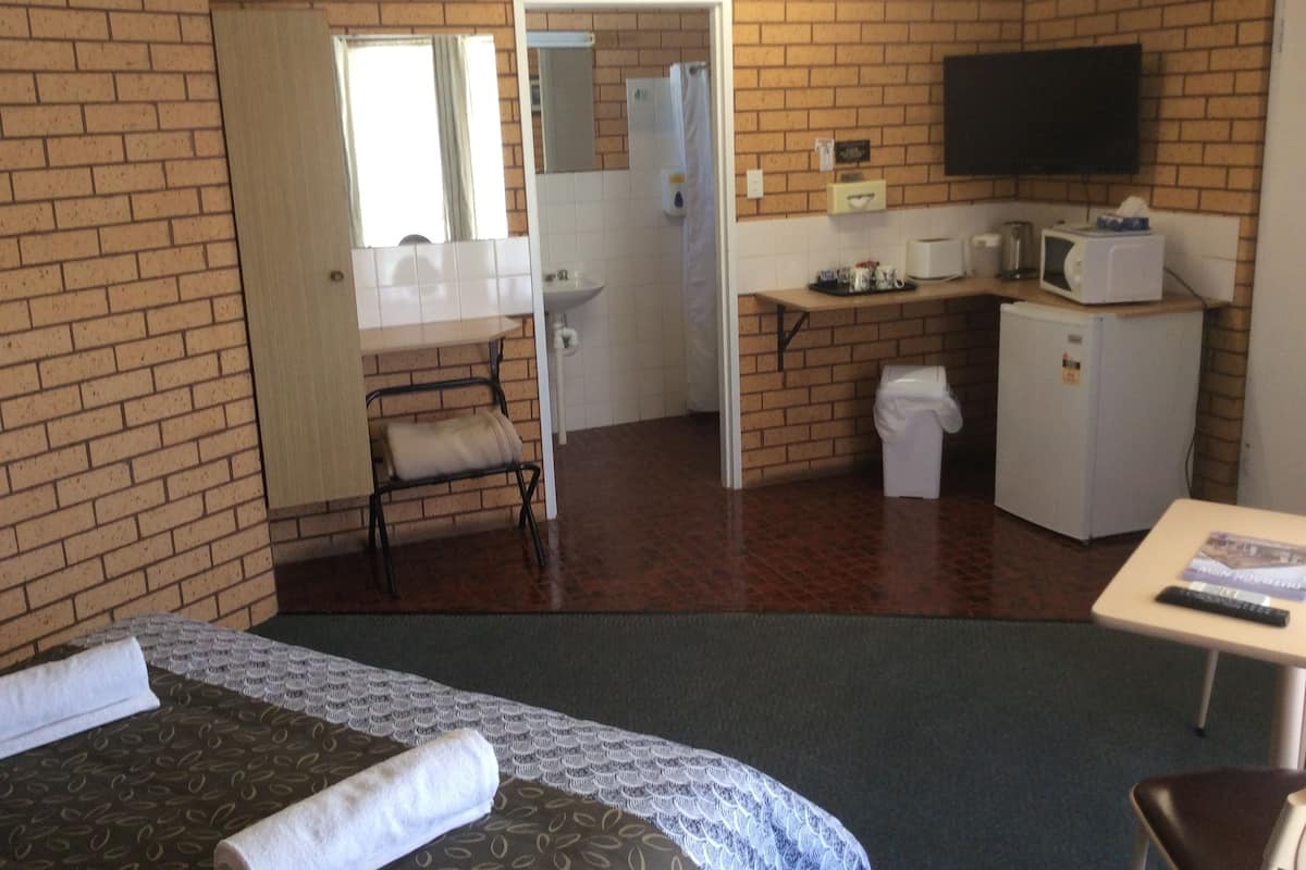 A hotel room with a brick wall, a bed with a patterned bedspread, a small table with a remote control, a microwave, and a refrigerator.