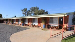 Un motel avec une série de chambres, un espace extérieur aménagé avec des sièges et un parking en gravier.