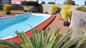 Une piscine bordée de rouge, entourée d’une terrasse en briques et agrémentée de plantes en pot.