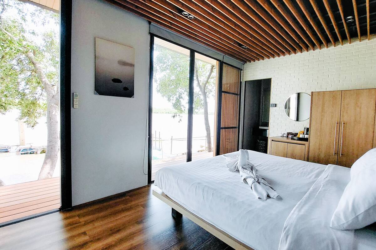 Een moderne slaapkamer met een groot bed, houten plafond en uitzicht op de omgeving.