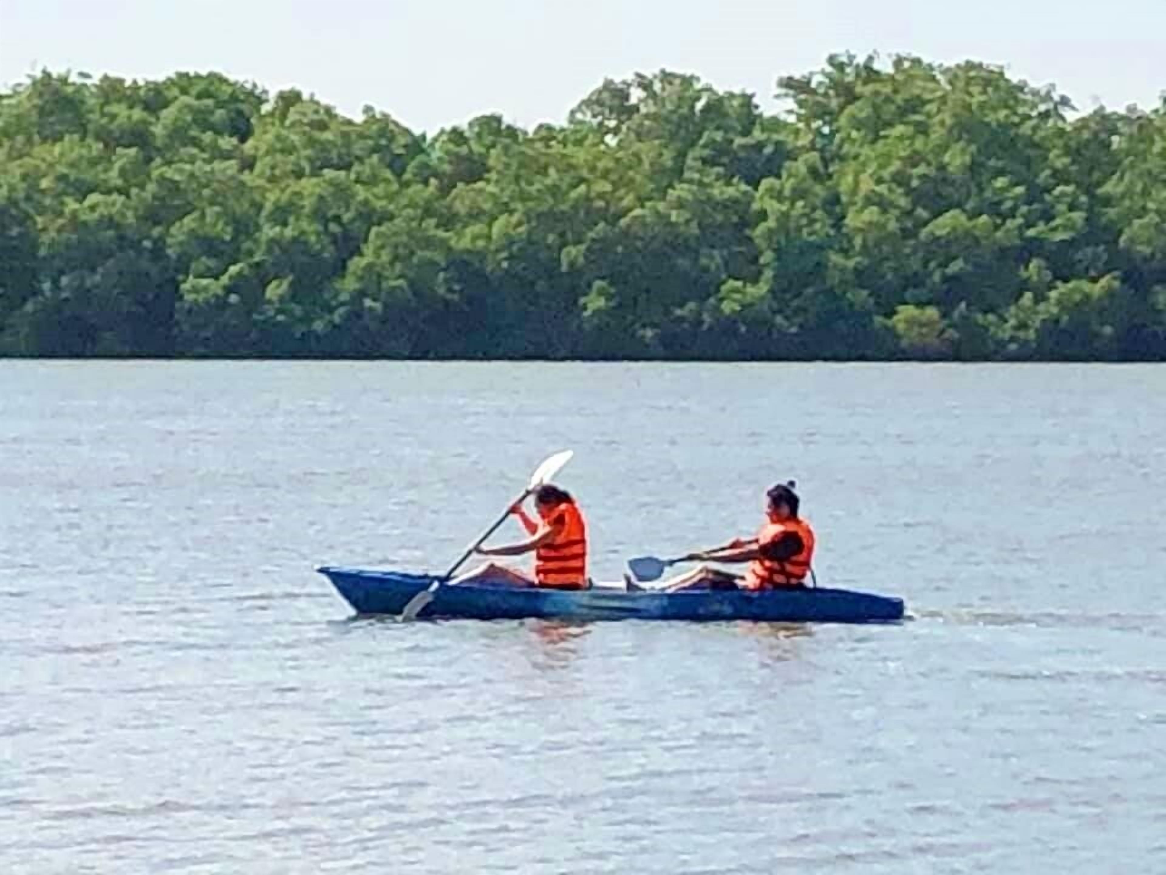 Two people in a blue boat on a calm body of water with a forested shoreline in the background.