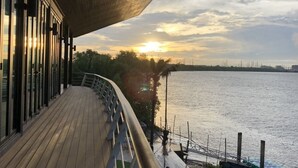 Een houten terras met een leuning, uitkijkend over een wateroppervlak tijdens de zonsondergang.