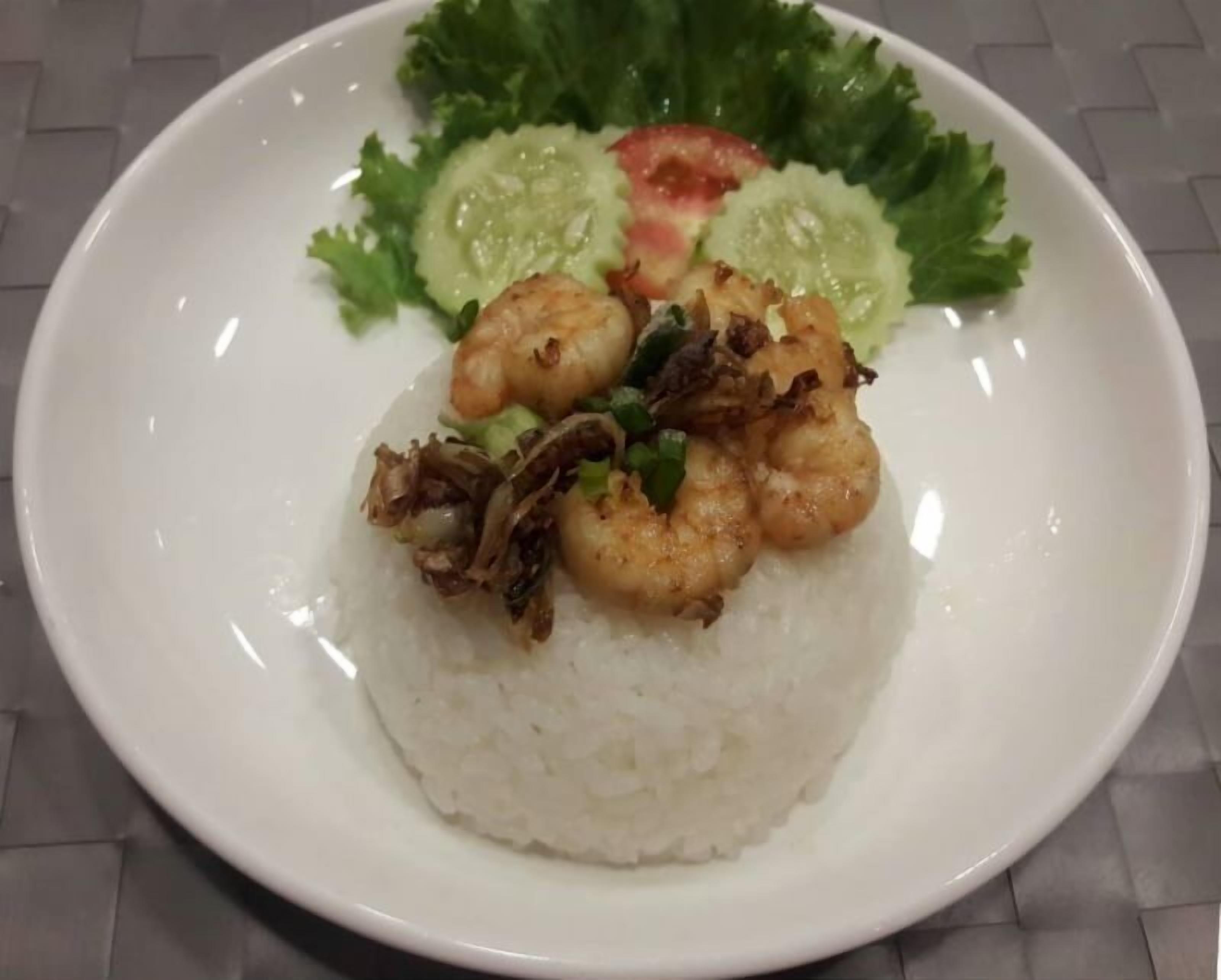 A plate of white rice topped with shrimp and fried onions, garnished with lettuce and cucumber slices.