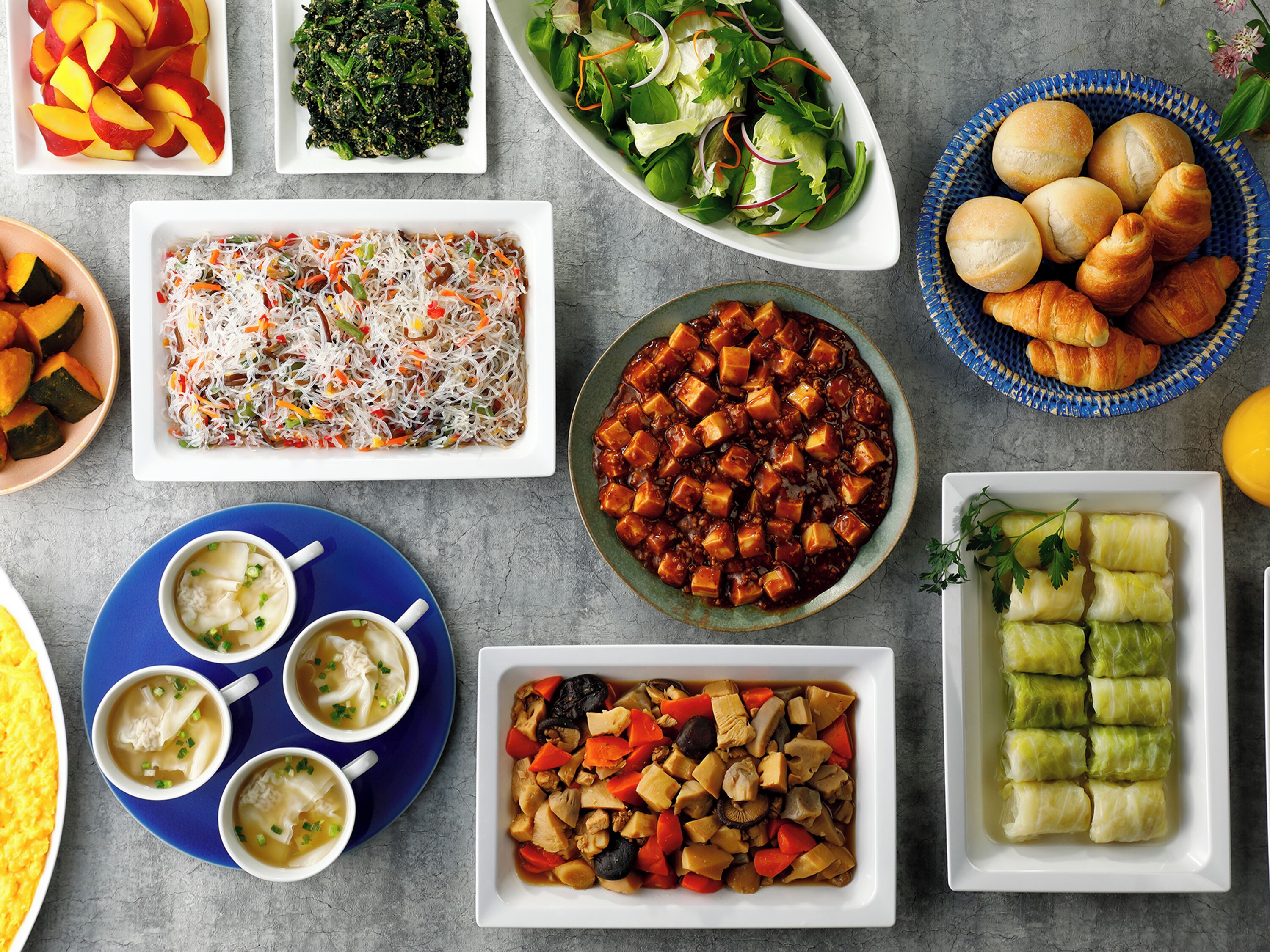 A variety of dishes including salads, soups, and rolls, arranged on a table.
