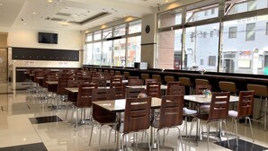 A cafeteria with multiple tables and chairs, large windows, and a clock on the wall.