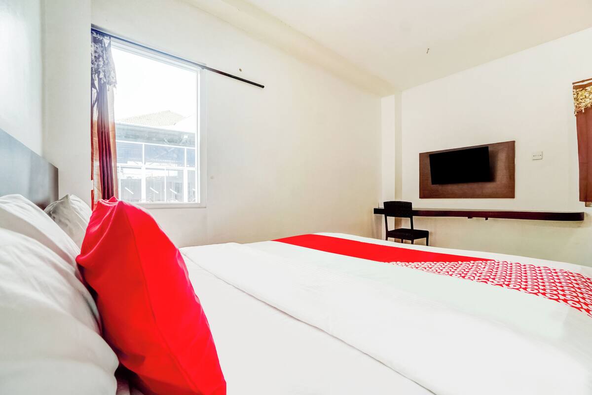 Quarto de hotel com cama, televisão presa à parede e janela com cortinas.