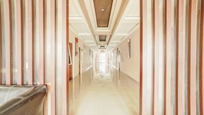 A long, narrow hallway with a reflective floor and vertical wooden panels on the walls. - Hotel O Siwalankerto Near Surabaya Carnival (Surabaya)