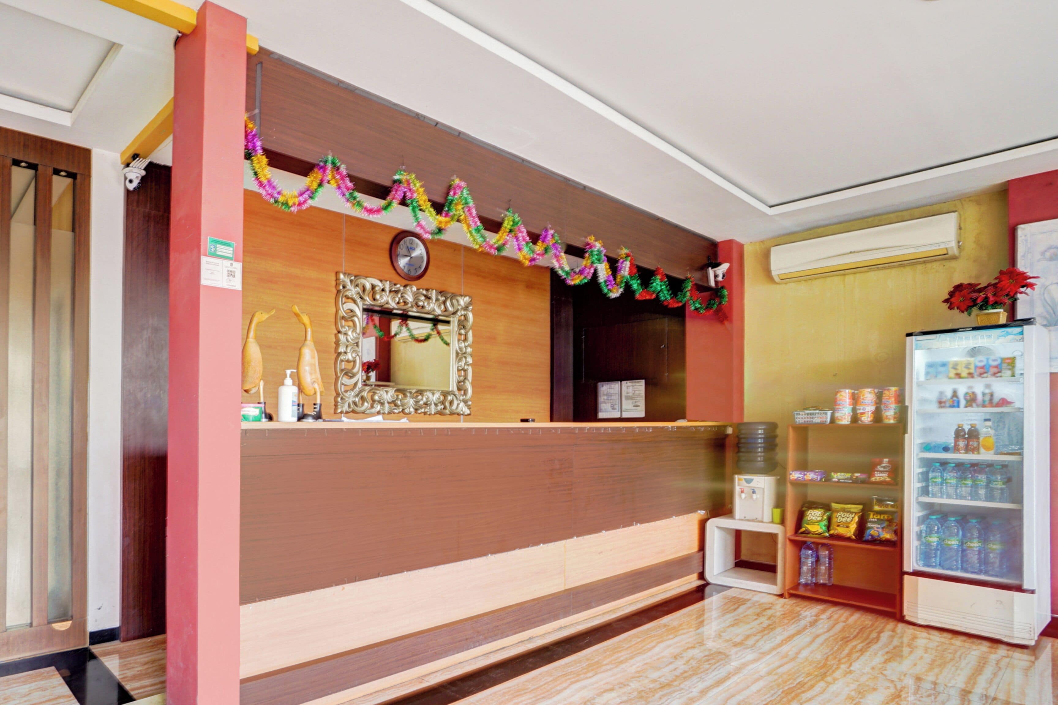 A reception area with a wooden counter, a mirror, a clock, and a refrigerator stocked with beverages.