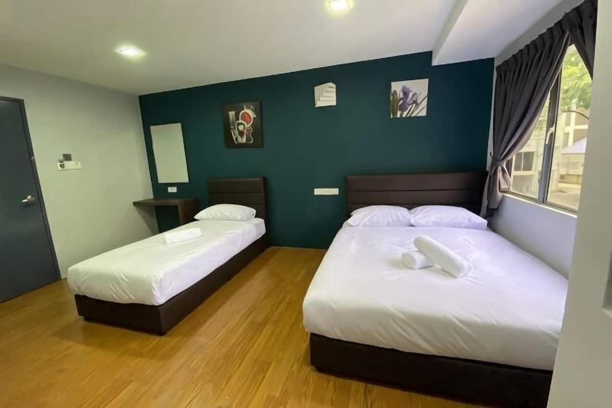 Quarto de hotel com duas camas de solteiro, piso de madeira, cabeceira escura, janela com cortinas e parede azul-turquesa.