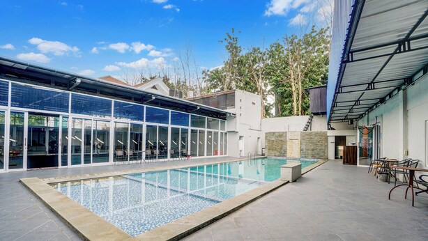 A modern indoor swimming pool with glass walls, a stone-tiled deck, and outdoor seating. - Hotel O Siwalankerto Near Surabaya Carnival (Surabaya)
