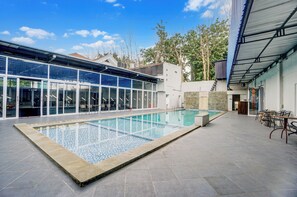 A modern indoor swimming pool with glass walls, a stone-tiled deck, and outdoor seating. - Hotel O Siwalankerto Near Surabaya Carnival (Surabaya)