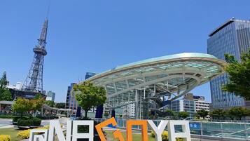 A modern building with a glass facade and a unique roof structure, surrounded by greenery and urban buildings.