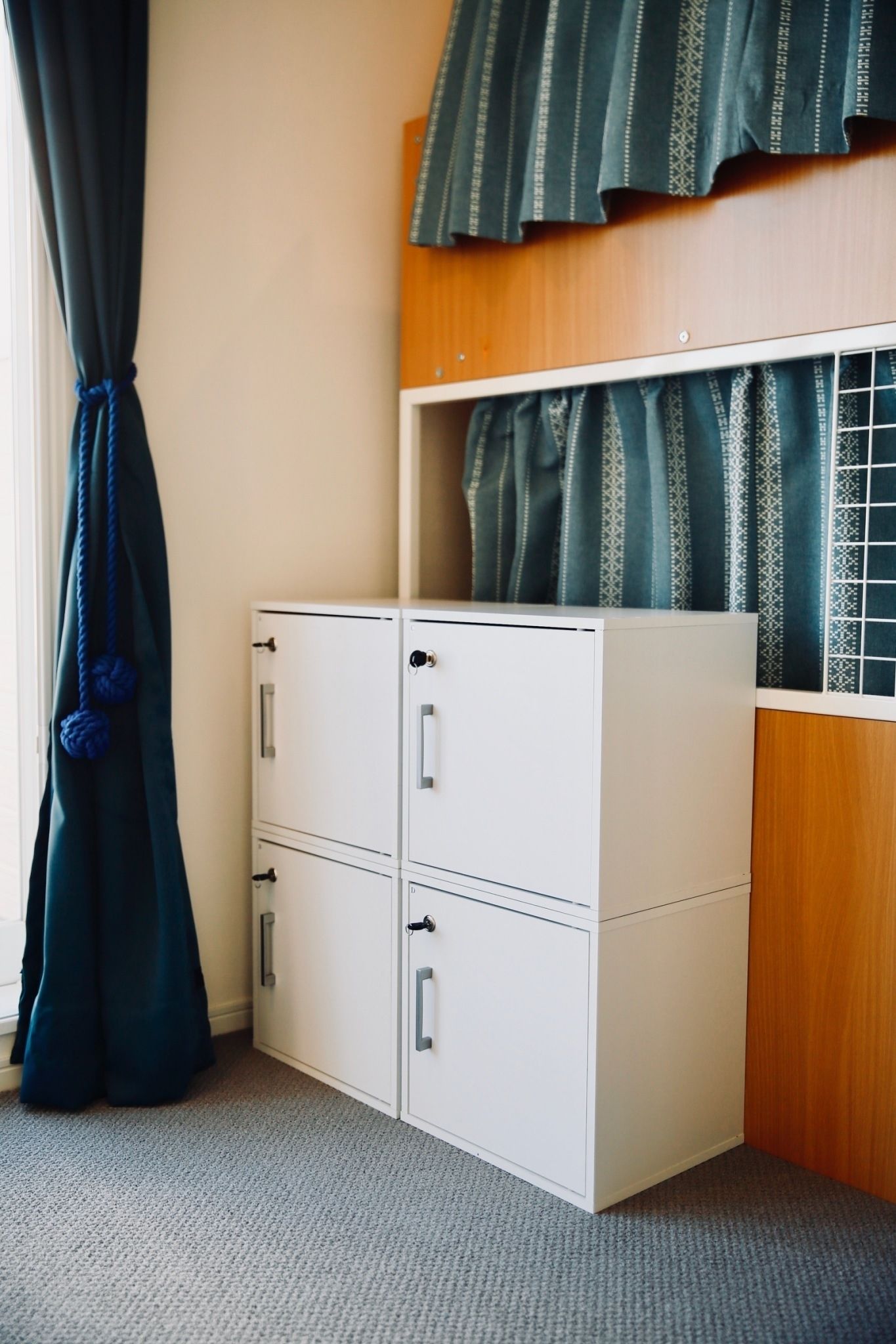 Une chambre avec un lit superposé, un meuble de rangement blanc et une fenêtre avec des rideaux.