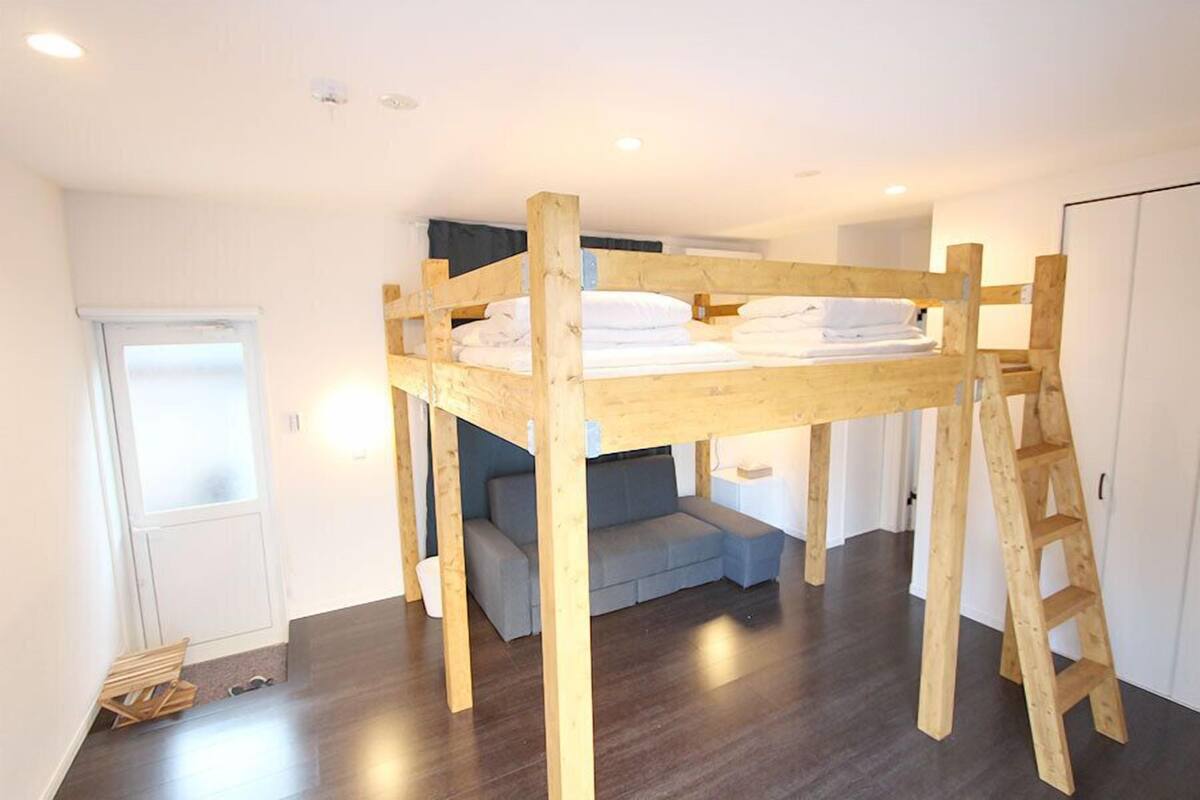 A room with a bunk bed, a gray sofa, a ladder, and a door.