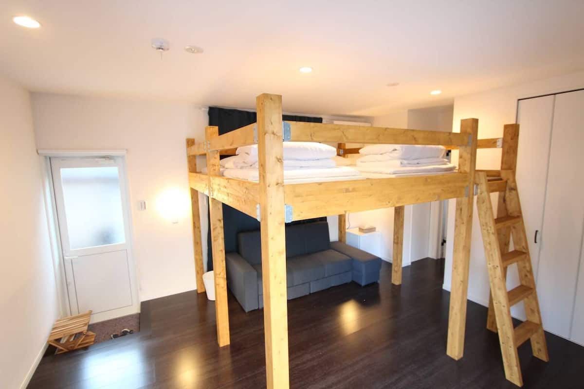 A bunk bed with a ladder, a sofa, and a wardrobe in a room with wooden flooring and white walls.