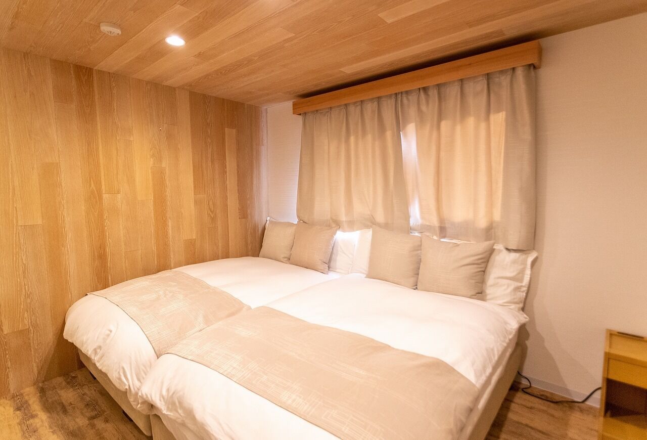 Quarto com teto de madeira, uma cama grande com roupa de cama branca, mesa de cabeceira de madeira e uma janela com cortinas.