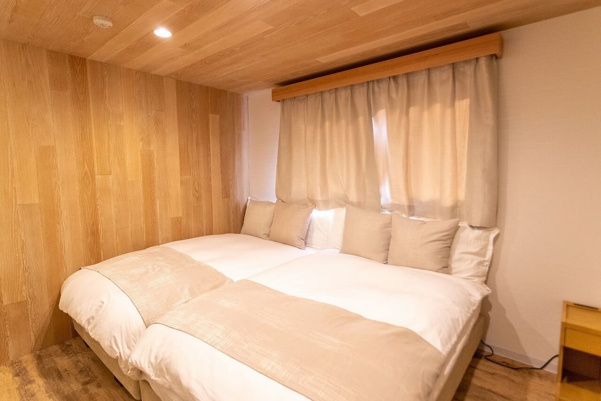 Une chambre avec un plafond en bois, un grand lit avec une literie blanche, une table de chevet en bois et une fenêtre avec des rideaux.