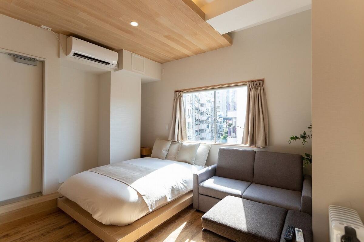 Une chambre à coucher comprenant un lit, un canapé, une fenêtre avec des rideaux, un climatiseur et un radiateur.