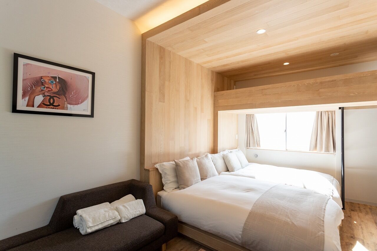 Quarto de hotel moderno com uma cama grande, um sofá pequeno, uma obra de arte emoldurada na parede e uma janela com cortinas.