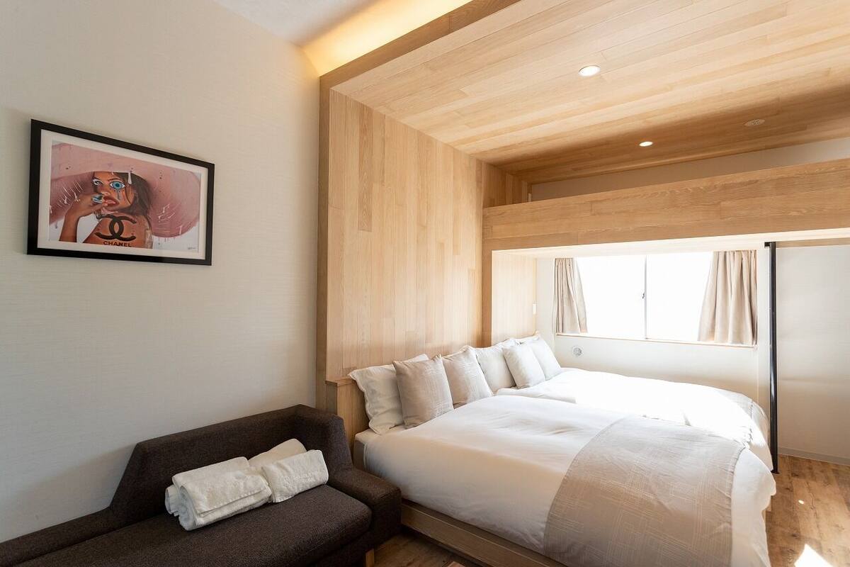 Une chambre d’hôtel moderne avec un grand lit, un petit canapé, une œuvre d’art encadrée au mur et une fenêtre avec des rideaux.