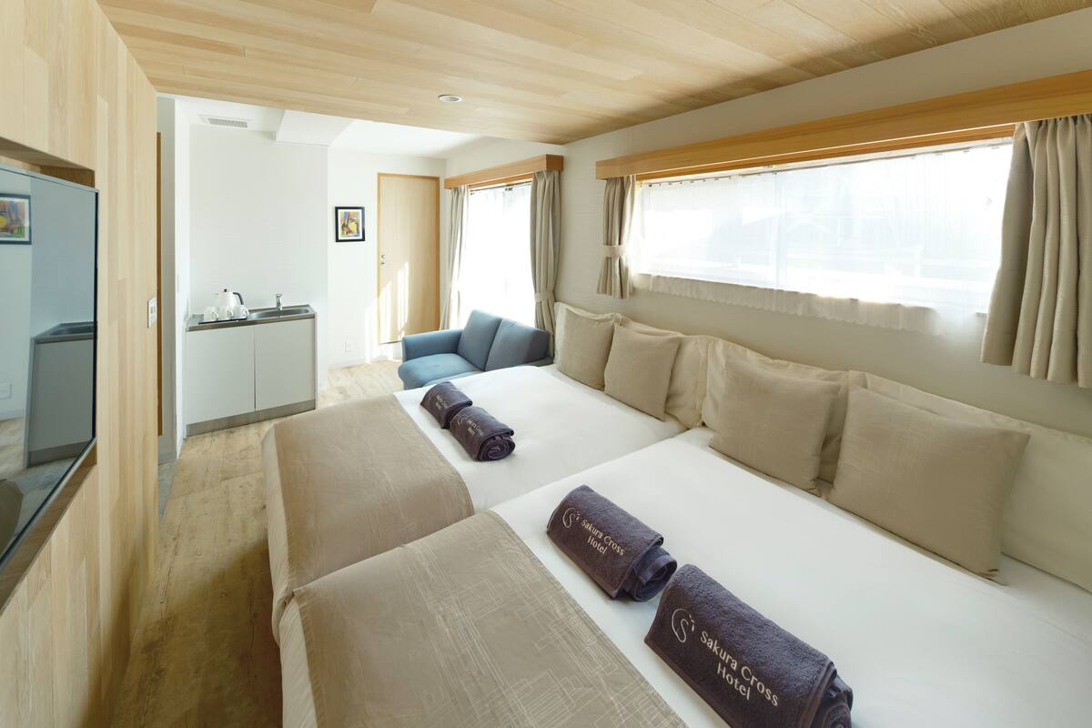 Une chambre d’hôtel avec un lit, un canapé, une petite kitchenette et une fenêtre avec des rideaux.