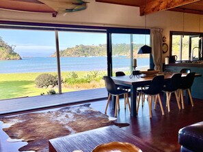 Un comedor con una mesa grande y sillas, vista al mar y una cocina con estufa y fregadero.