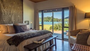 Ein Schlafzimmer mit einem großen Bett, einer Bank, einem Sessel und Seeblick durch eine Schiebetür.