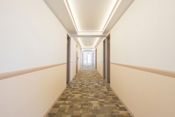 A hotel hallway with carpeted flooring, white walls, and doors on both sides.