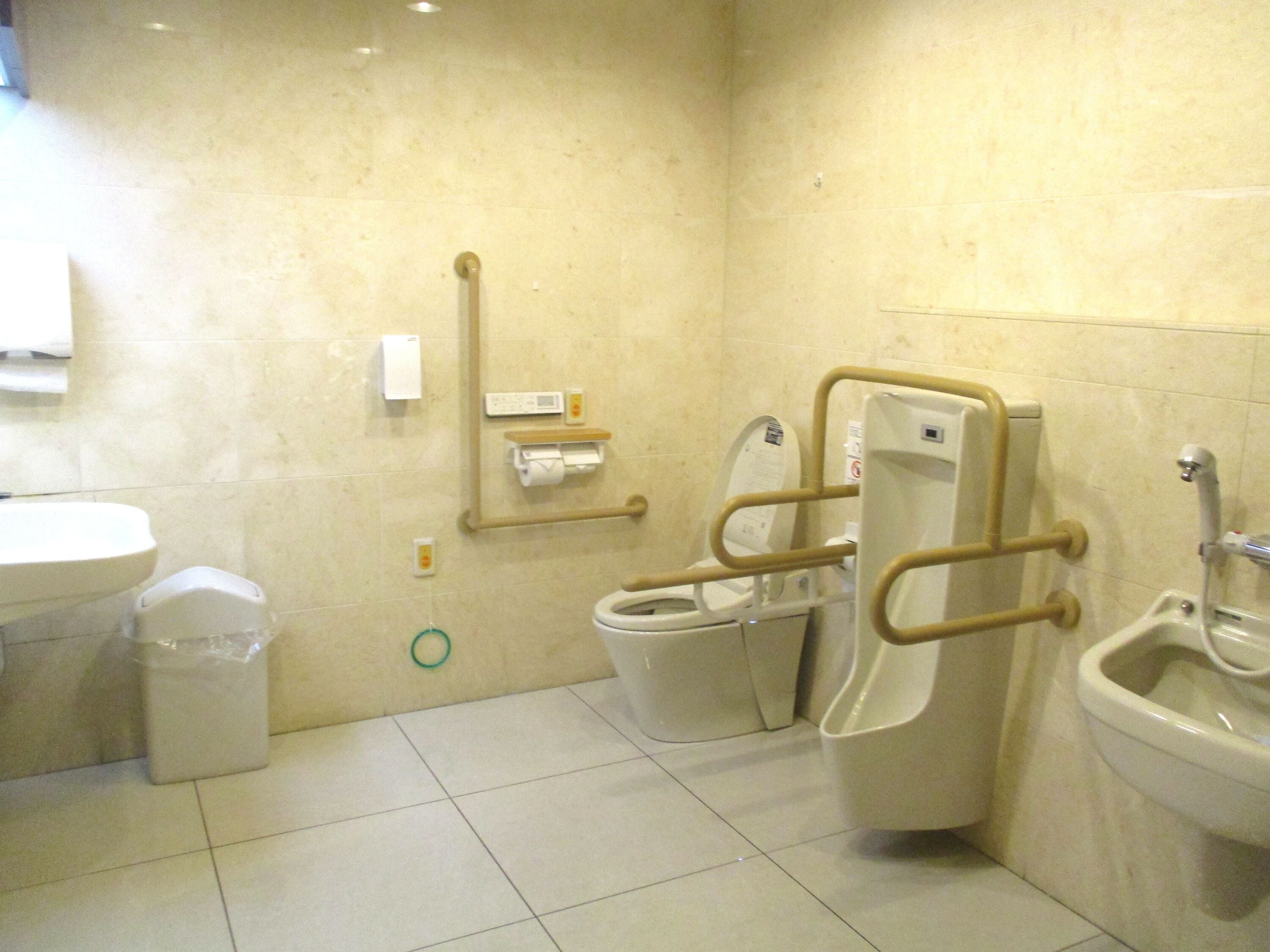 A bathroom with two toilets, a bidet, a sink, and a trash bin.
