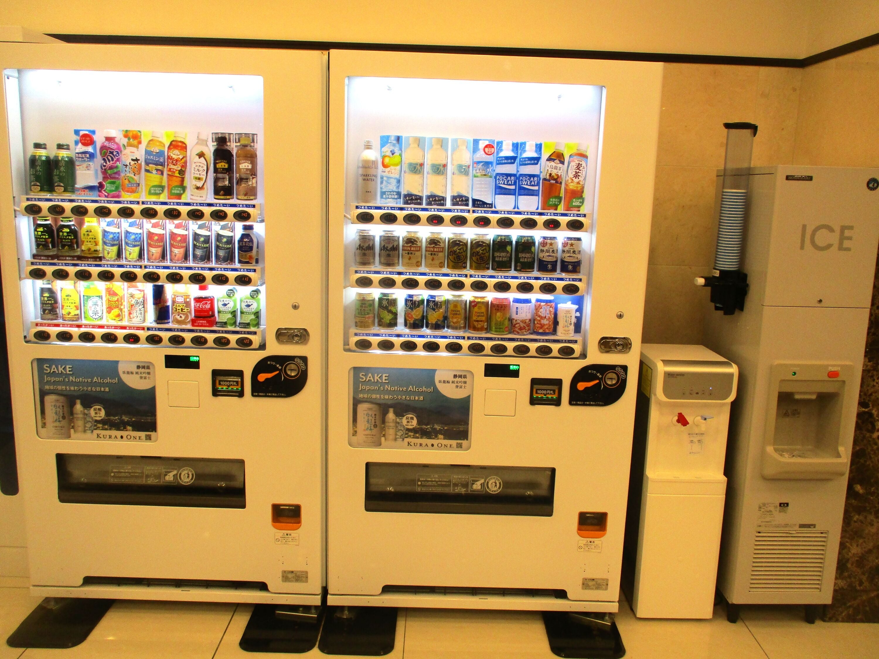 Dos máquinas expendedoras de bebidas con una variedad de opciones y un dispensador de agua etiquetado como 'ICE' a la derecha.