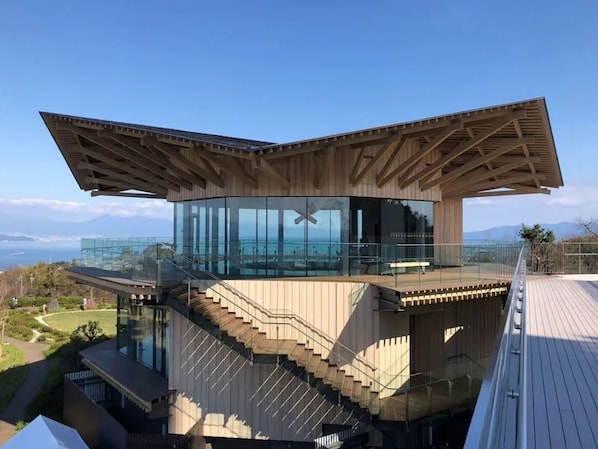 Un edificio moderno con cerramiento de vidrio, terraza de madera y una escalera que lleva a un nivel superior.