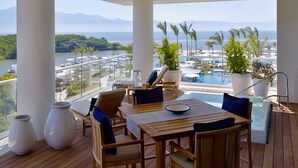 A wooden deck with a table and chairs, overlooking a pool and a scenic view of a body of water and mountains.